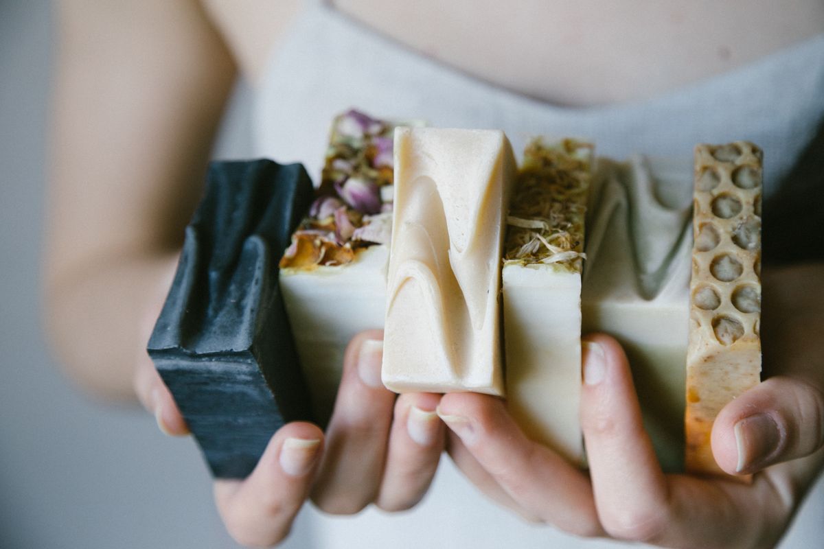 Hands holding a stack of artisan soap bars with botanicals